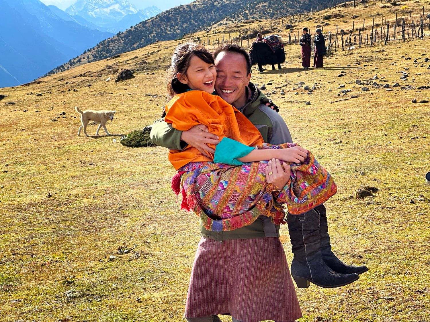 A woman of Laya carrying a child, with yaks on the slope behind, Bhutan