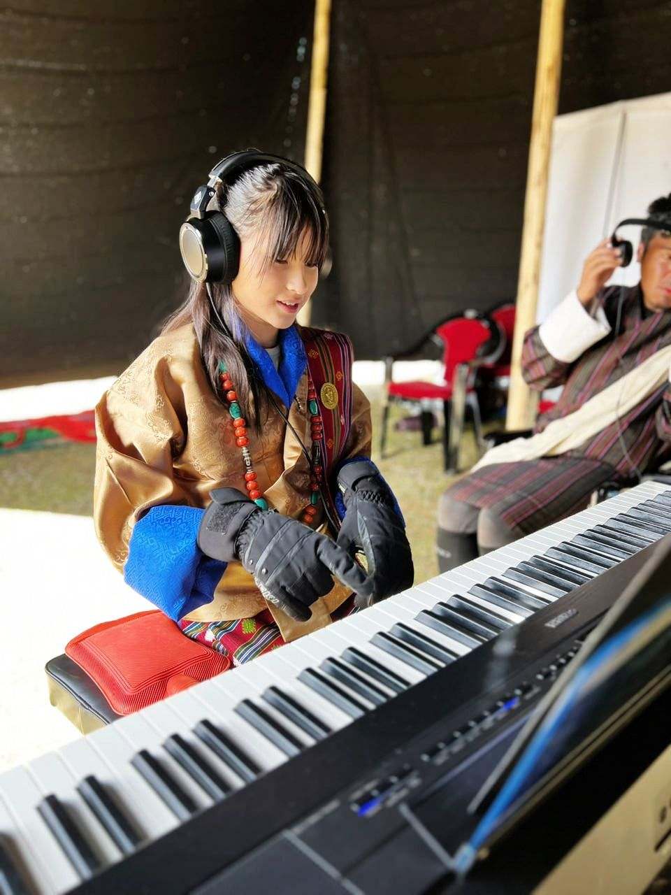 Hillary O’Sullivan at the keyboard in Bhutanese dress at the Royal Highland Festival, Laya, from The Girl and Her Piano